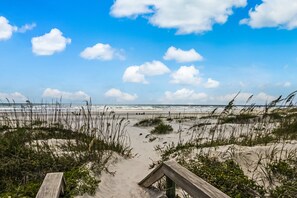 A beach with a wooden boardwalk leading to the water, sandy dunes, and a clear sky with clouds. - SunLounger|3BR/2BA Beachfront Retreat (Saint Augustine Beach)