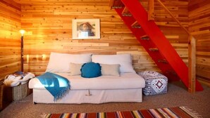 A wooden cabin interior with a white sofa, a red staircase, and a framed picture on the wall.