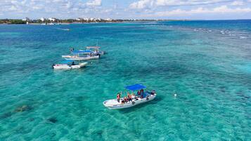 A clear view of a coastal area with several boats anchored in shallow, turquoise waters.