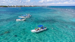 A clear view of a coastal area with several boats anchored in shallow, turquoise waters.