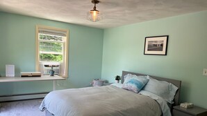 A bedroom with a bed, bedside tables, a desk with a computer, a window, and a ceiling light fixture.