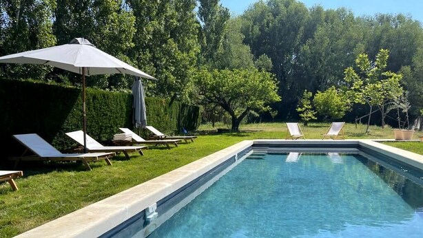 A rectangular swimming pool with a tiled edge, surrounded by a grassy area with several lounge chairs and a large umbrella. - Charming Mas in the countryside, near the village of Lambesc, large garden, (Lambesc)