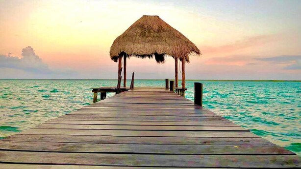A wooden pier leading to a thatched-roof structure over turquoise waters.
