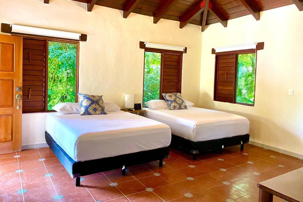 A room with two beds, wooden beams on the ceiling, and windows with shutters.