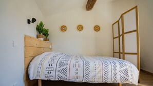 Una cama con colcha estampada, cabecera de madera, una planta en maceta y tres adornos circulares en la pared.