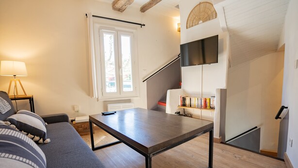 Una sala de estar moderna con un sofá, una mesa de centro, un televisor montado en la pared y una escalera que lleva a un nivel superior.