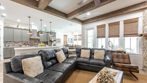 A modern living room with a black leather sectional sofa, a wooden coffee table with decorative items, and a kitchen in the background. - Summer Kickoff Special! Beach House on 30A, Steps from the Beach! (Santa Rosa Beach)