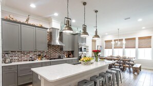 A modern kitchen with grey cabinets, a brick backsplash, and a central island with bar stools. - Summer Kickoff Special! Beach House on 30A, Steps from the Beach! (Santa Rosa Beach)