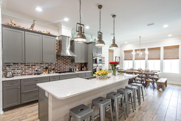 A modern kitchen with grey cabinets, a brick backsplash, and a central island with bar stools.