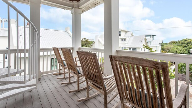 A wooden deck with white railings and rocking chairs, overlooking a residential area with white houses. - Summer Kickoff Special! Beach House on 30A, Steps from the Beach! (Santa Rosa Beach)