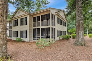 A two-story house with large windows and a covered porch, surrounded by trees and a wooded area.