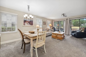 A spacious living room with a dining area, large windows, a ceiling fan, and a view of the outdoors.