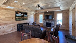 A cozy cabin interior with a stone fireplace, wooden walls, a ceiling fan, and a large window. - Beautiful rustic cabin on the shores of Greer's Ferry Lake (Higden)