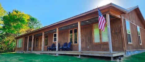 A wooden cabin with a porch, an American flag, and a lawn.