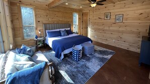 A cozy wooden cabin bedroom with a bed, a chair, a small table, and a ceiling fan. - Beautiful rustic cabin on the shores of Greer's Ferry Lake (Higden)