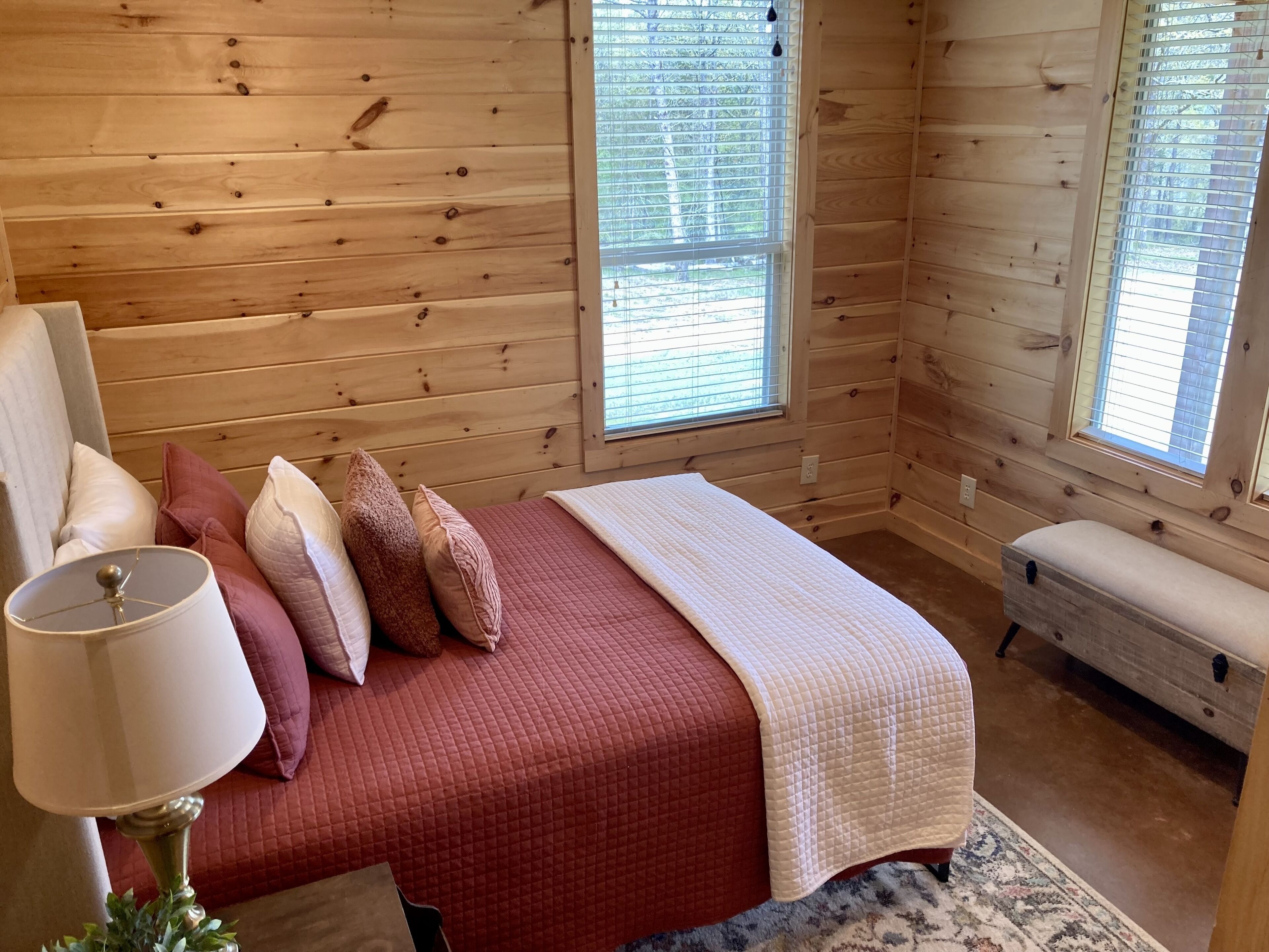 A wooden cabin bedroom with a bed, pillows, a bedside lamp, and a bench.