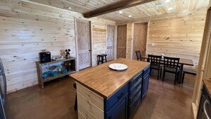 A wooden interior with a central island, a coffee machine, and a dining area with chairs and a table. - Beautiful rustic cabin on the shores of Greer's Ferry Lake (Higden)