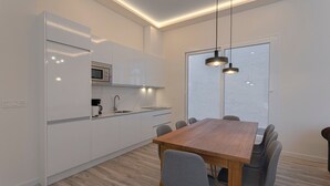 A modern kitchen with white cabinets, a wooden dining table, and a large window. - Fresh Velazquez Apartment E (Málaga)