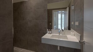 A modern bathroom with a large mirror, a white sink, and a shower area. - Fresh Velazquez Apartment E (Málaga)