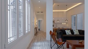 A spacious living area with a sofa, a wooden coffee table, and a dining table. A kitchen with modern appliances and pendant lighting is visible in the background. - Fresh Velazquez Apartment E (Málaga)