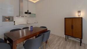 A modern kitchen with a wooden dining table, grey chairs, a built-in oven, and a cabinet with a light. - Fresh Velazquez Apartment D (Málaga)