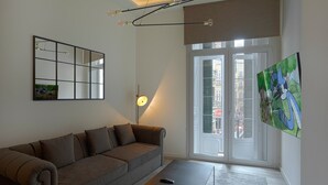 A modern living room with a sofa, a coffee table, a floor lamp, a large mirror, and a window with a view of buildings. - Fresh Velazquez Apartment D (Málaga)