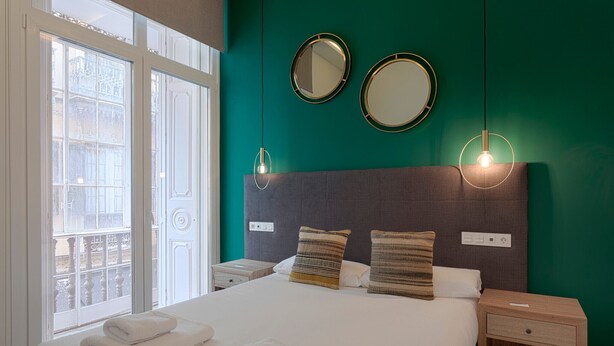 A hotel room with a large bed, two bedside tables, a nightstand, and two wall-mounted mirrors. - Fresh Velazquez Apartment D (Málaga)