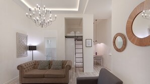 A modern living room with a tufted sofa, a grey armchair, a chandelier, and a large mirror. - Fresh Velazquez Apartment B (Málaga)