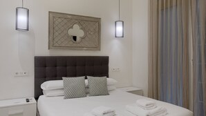 A neatly made bed with white linens and two patterned pillows, a grey upholstered headboard, and a wall-mounted decorative piece above it. - Fresh Velazquez Apartment B (Málaga)