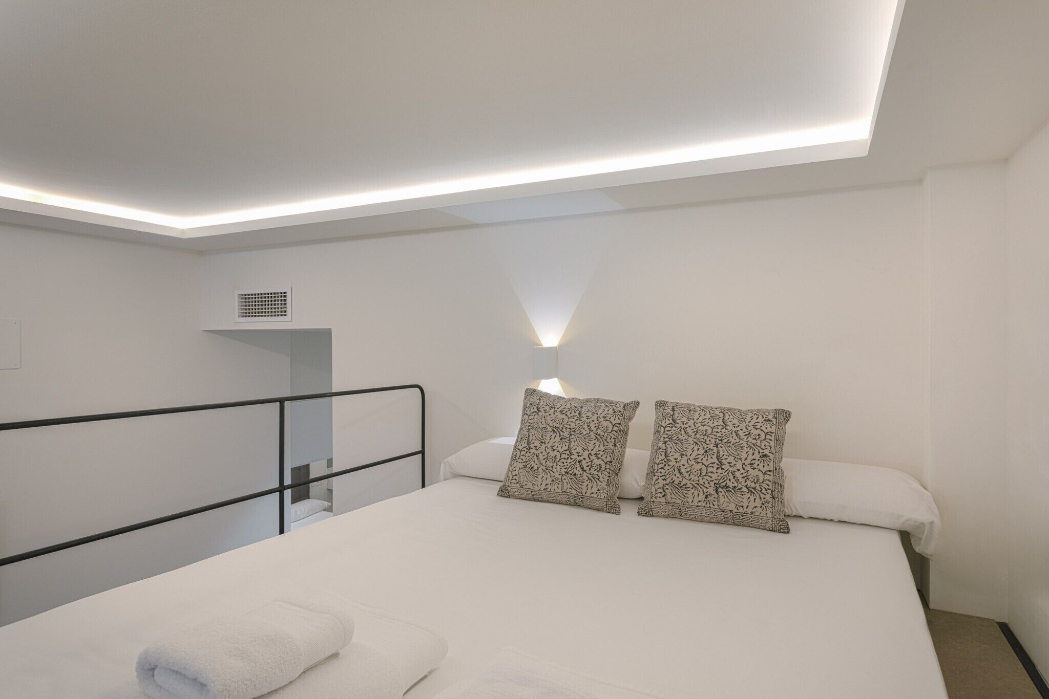 A modern bedroom with a large bed, two patterned pillows, a white blanket, and a ceiling light.