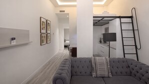 A modern living room with a grey sofa, a ladder, and a bunk bed in the background. - Fresh Velazquez Apartment C (Málaga)
