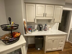 Una cocina con armarios blancos, una encimera de mármol, una cafetera, un cubo de basura y un adorno en la encimera.