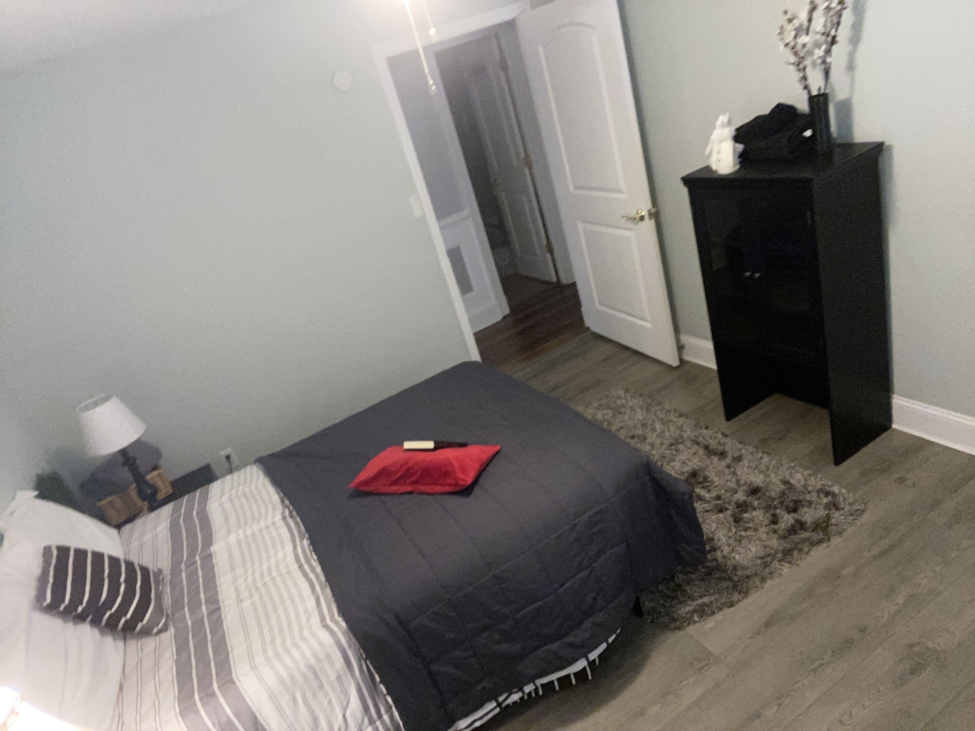 Un dormitorio con cama, mesita de noche, cómoda y puerta que da a otra habitación.