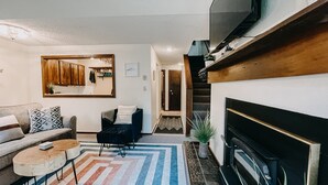 A living room with a sofa, coffee table, and fireplace. There is a mirror on the wall and a staircase leading to another room. - 73SW - F/P - W/D - Sleeps 6 (Deming)