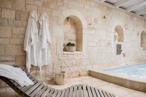 A stone-walled indoor pool area with wooden loungers and white towels hanging on the wall. - Trullo Panoramico - Micele Holiday Houses (Locorotondo)