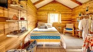 Acogedora habitación de cabaña de madera con cama, sillón, perchero y estante con señal de WiFi.