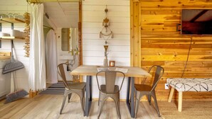 Un interior de madera con una mesa de comedor, sillas, un televisor montado en la pared y techo de madera.