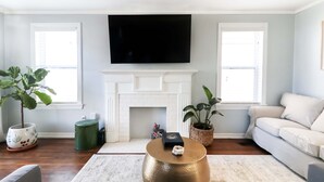 A living room with a fireplace, a flat-screen TV mounted above it, a sofa, and two potted plants.