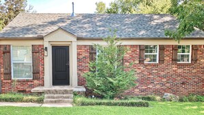 A brick house with a black front door, a small front yard, and a tree.