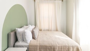 A neatly made bed with a beige quilt, a white pillow, and a headboard against a light green wall.