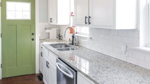 A kitchen with white cabinets, a green door, and a patterned rug.