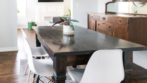 A dining area with a dark wooden table, white chairs, a chandelier, and a wooden cabinet with a mirror.