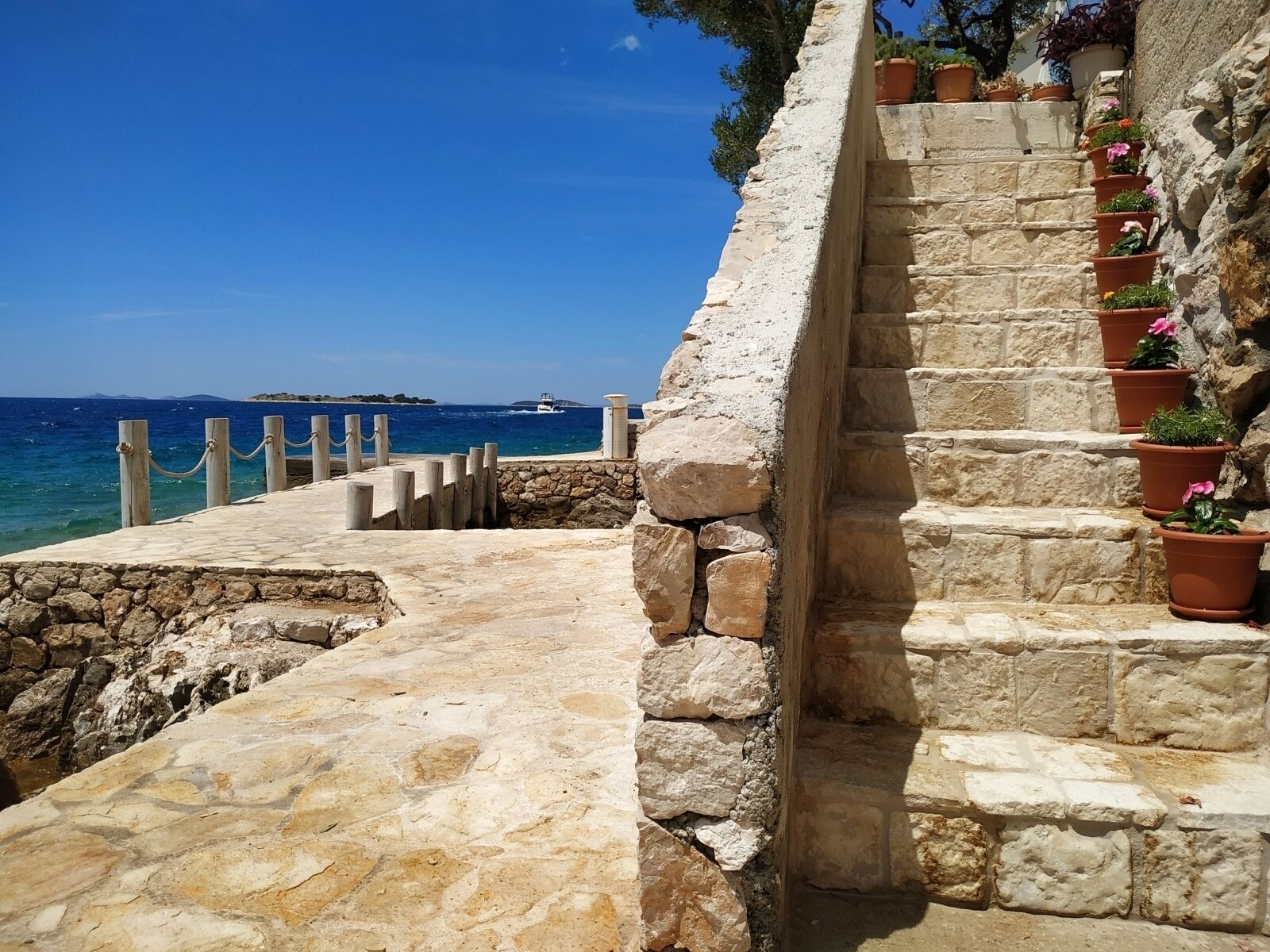 Eine Steintreppe führt zu einer Küstenregion mit freiem Blick auf das Meer und eine entfernte Insel.