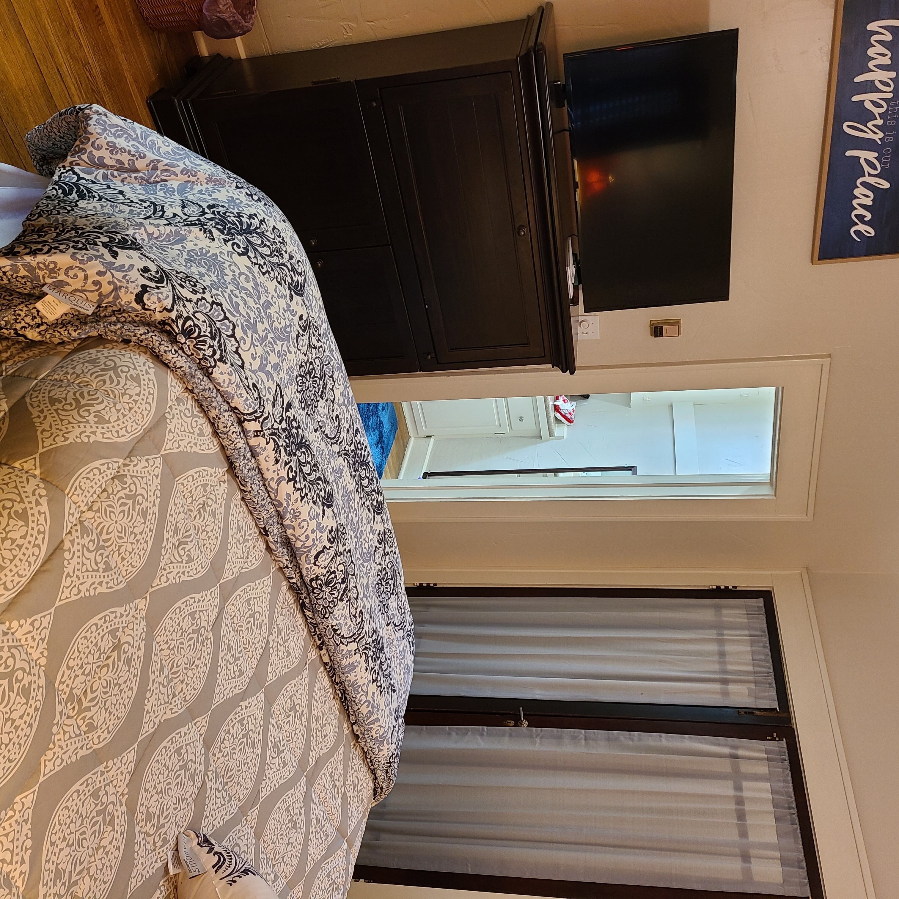 A bedroom with a bed, a television on a dresser, a door, and a window with curtains.