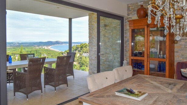 Un comedor con vista al mar, sillas de mimbre, una mesa de madera y una araña.