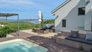Zona de piscina con sillas de descanso y una pérgola, con vistas a un paisaje pintoresco.