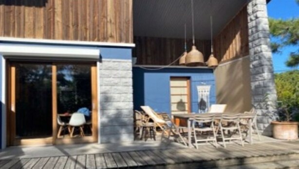A wooden deck with outdoor furniture, a stone pillar, and a blue building facade. - Villa (Lège-Cap-Ferret)