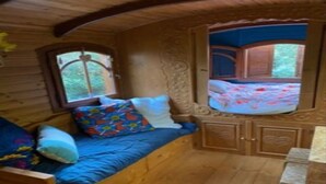 A cozy cabin interior with a wooden bed, a built-in bench with cushions, and a window with a view of the outdoors. - Villa (Lège-Cap-Ferret)