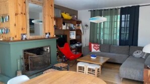 A cozy living room with a fireplace, a bookshelf, a red chair, a grey sofa, and a table. - Villa (Lège-Cap-Ferret)