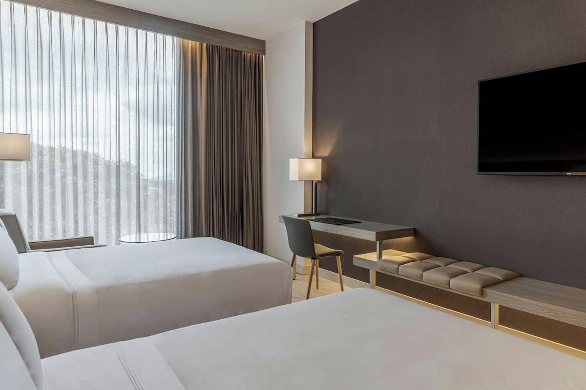 Hotelkamer met twee bedden, een bureau, een stoel, een televisie en een raam met gordijnen.
